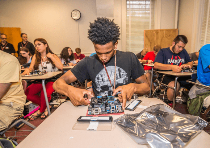 Student sitting in classroom working on computer hardware.