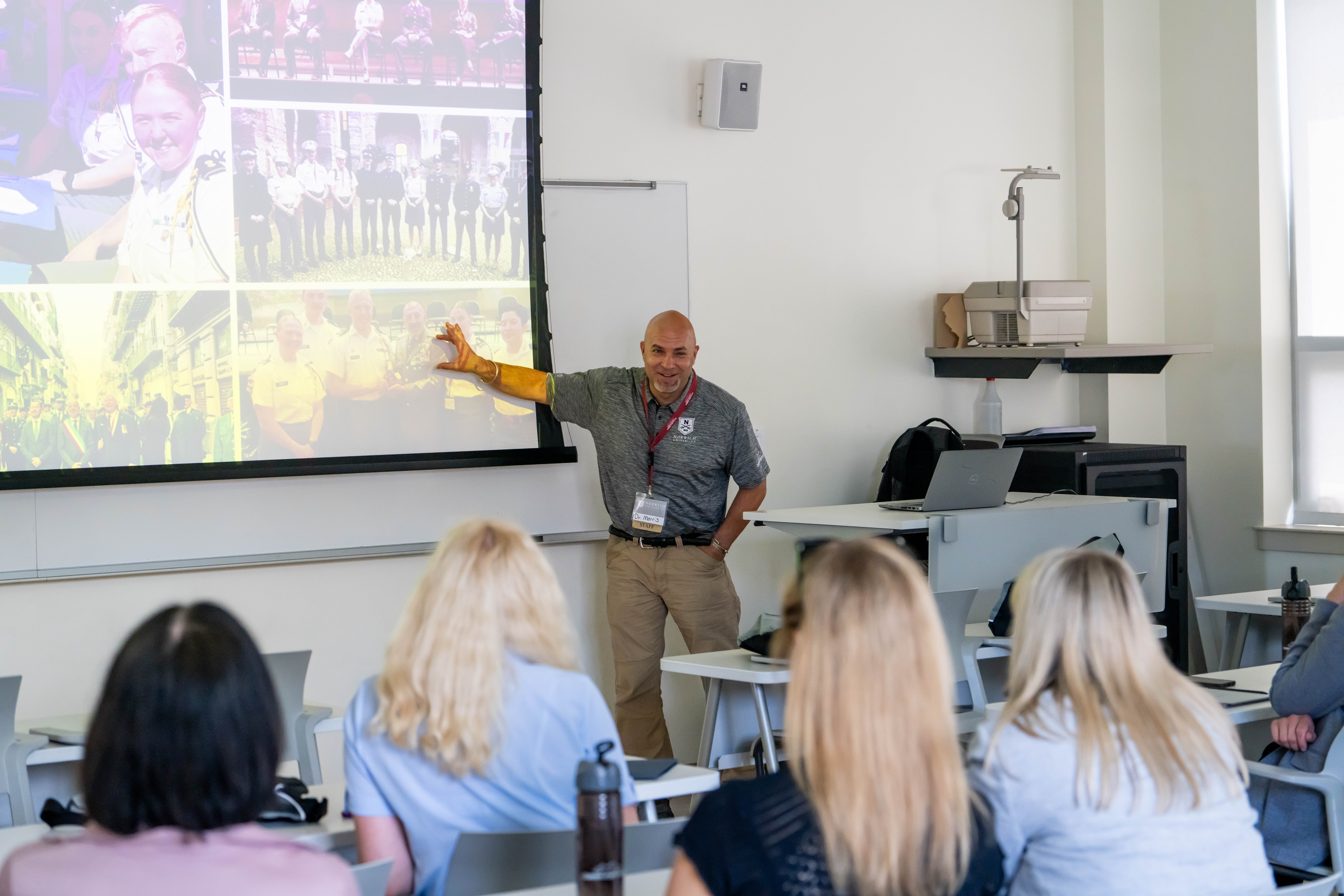 Dr. Travis Morris points to the screen during a presentation to the seated Latvian government officials in the audience.