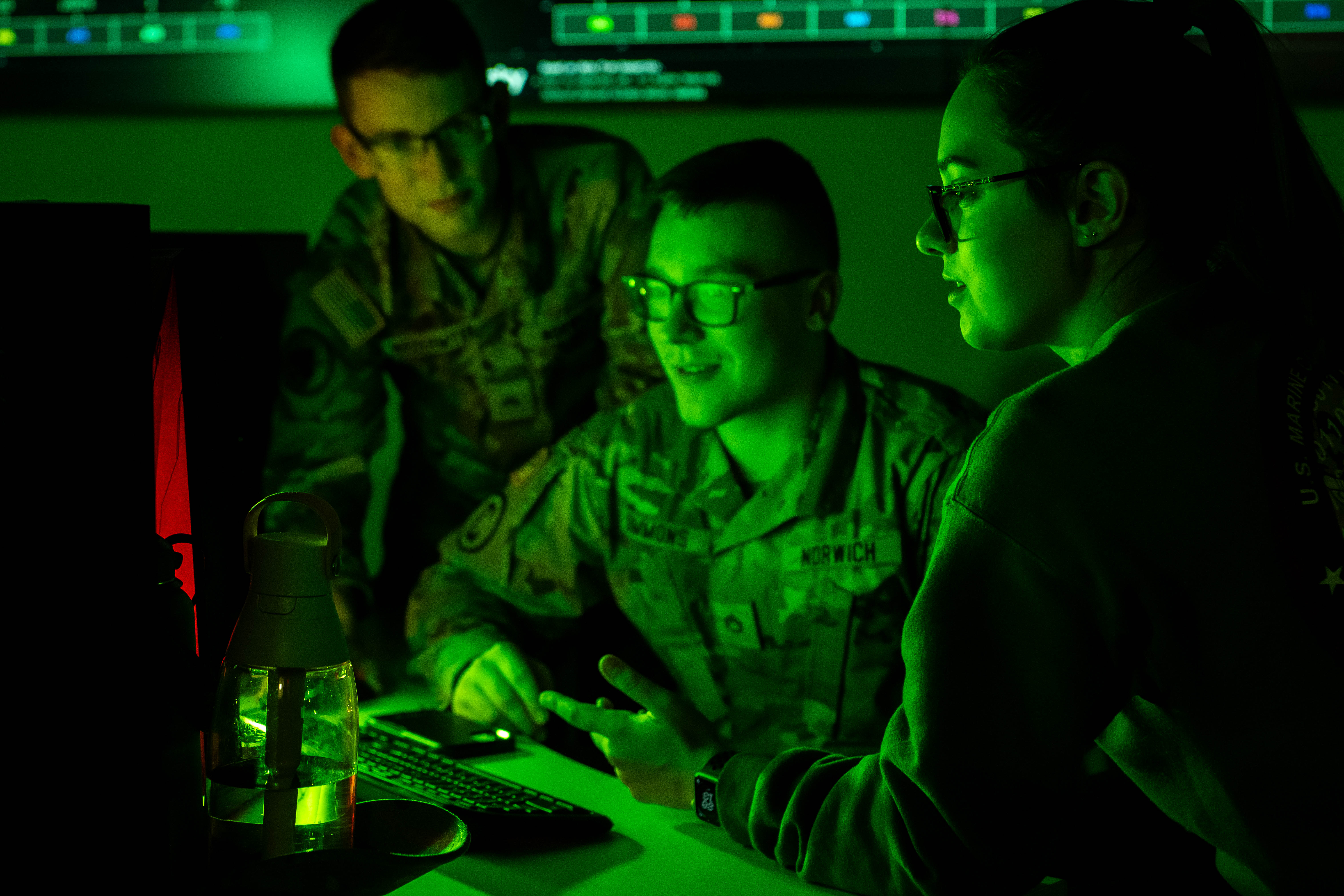 Three students in front of a computer in the Norwich University Cyber War Room.