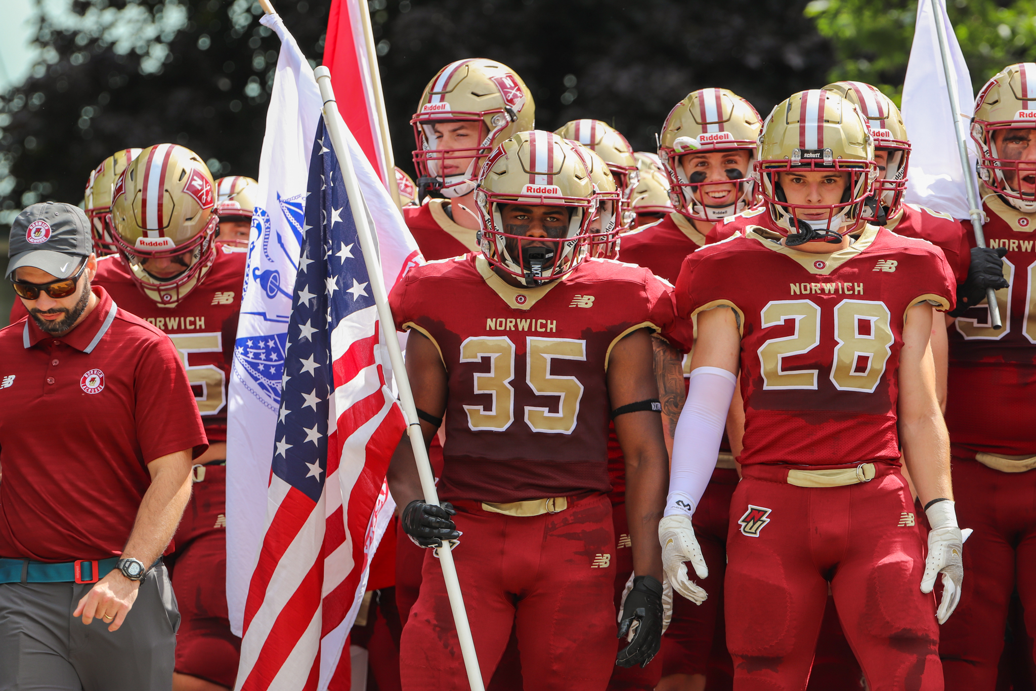 Jehric hackney stands in the center of his team while holding an American flag and preparing to run onto the football field.