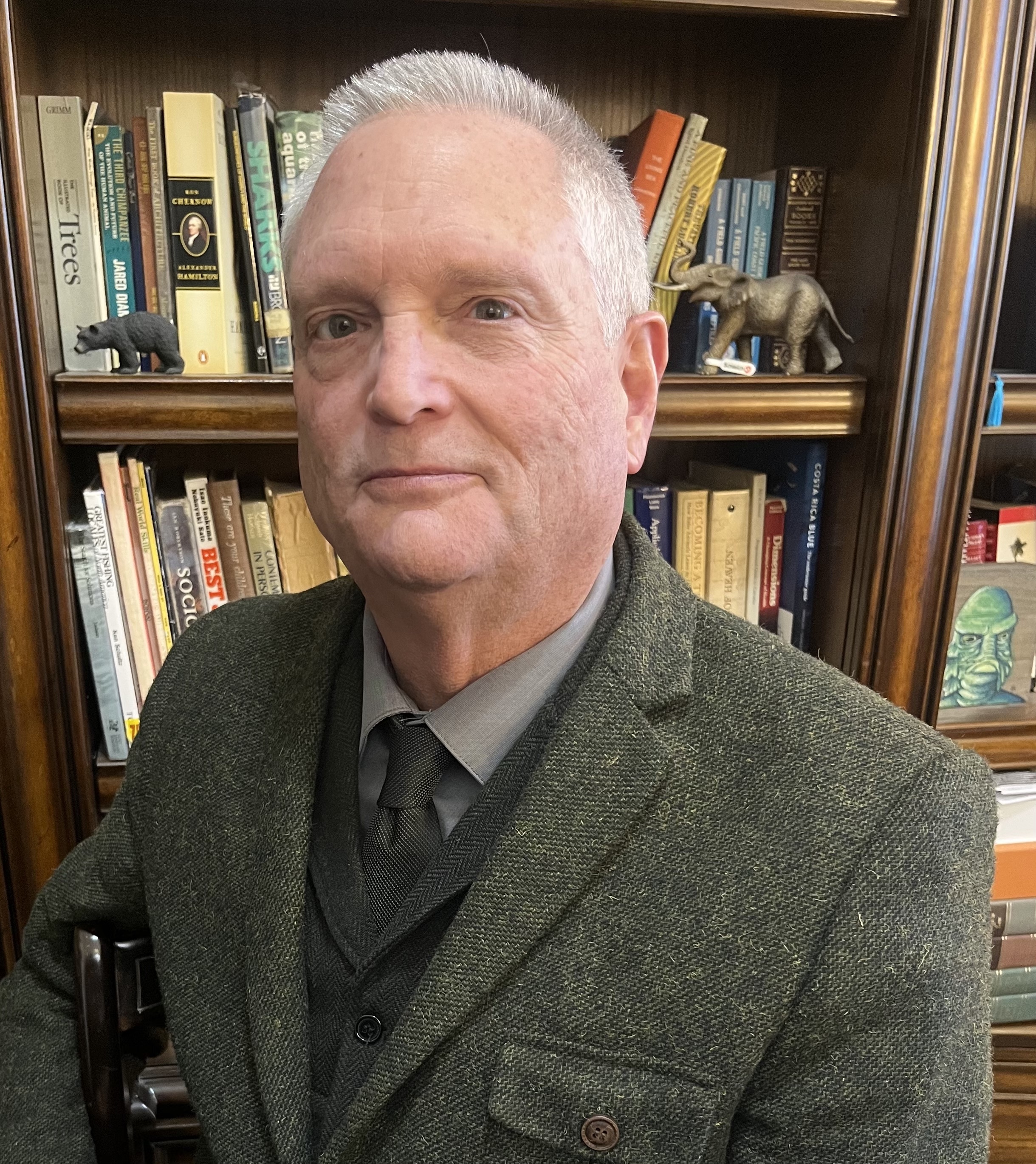 A photo of Dr. Marvin Lutnesky in a suit and tie in front of a bookcase with books and a small elephant statue.