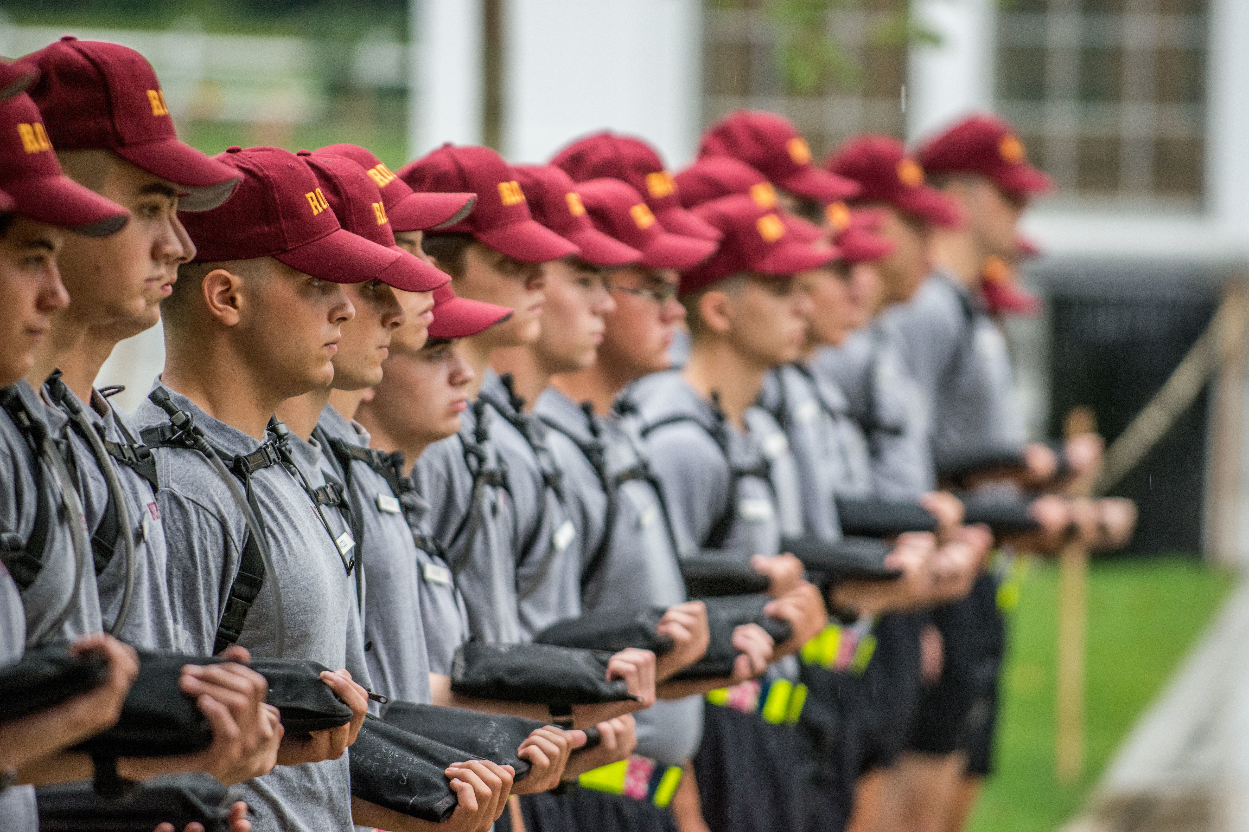 A group of Rooks stand in a line, all wearing grey shirts, maroon Rook hats, and holding shirts.