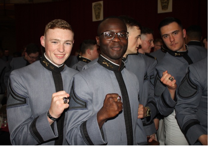 Group of cadets in uniform showing their rings at a formal event.
