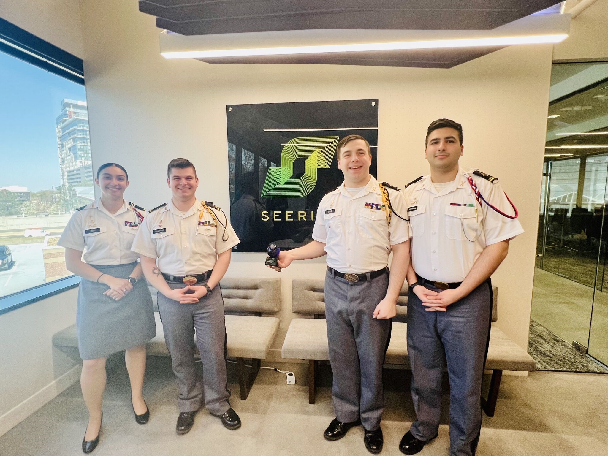 Isabella Ross, Jayden LaVecchia, Brendan Coyne, and Ahmed Mohammad stand in front of the Seerist logo on the wall in Seerist HQ; LaVecchia is displaying the trophy in his right hand.