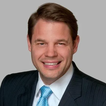 A formal headshot of Paul Fousek in a suit.