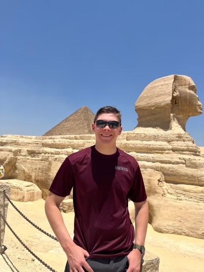 Person in sunglasses and a t-shirt standing in front of the Sphinx and a pyramid in Egypt.
