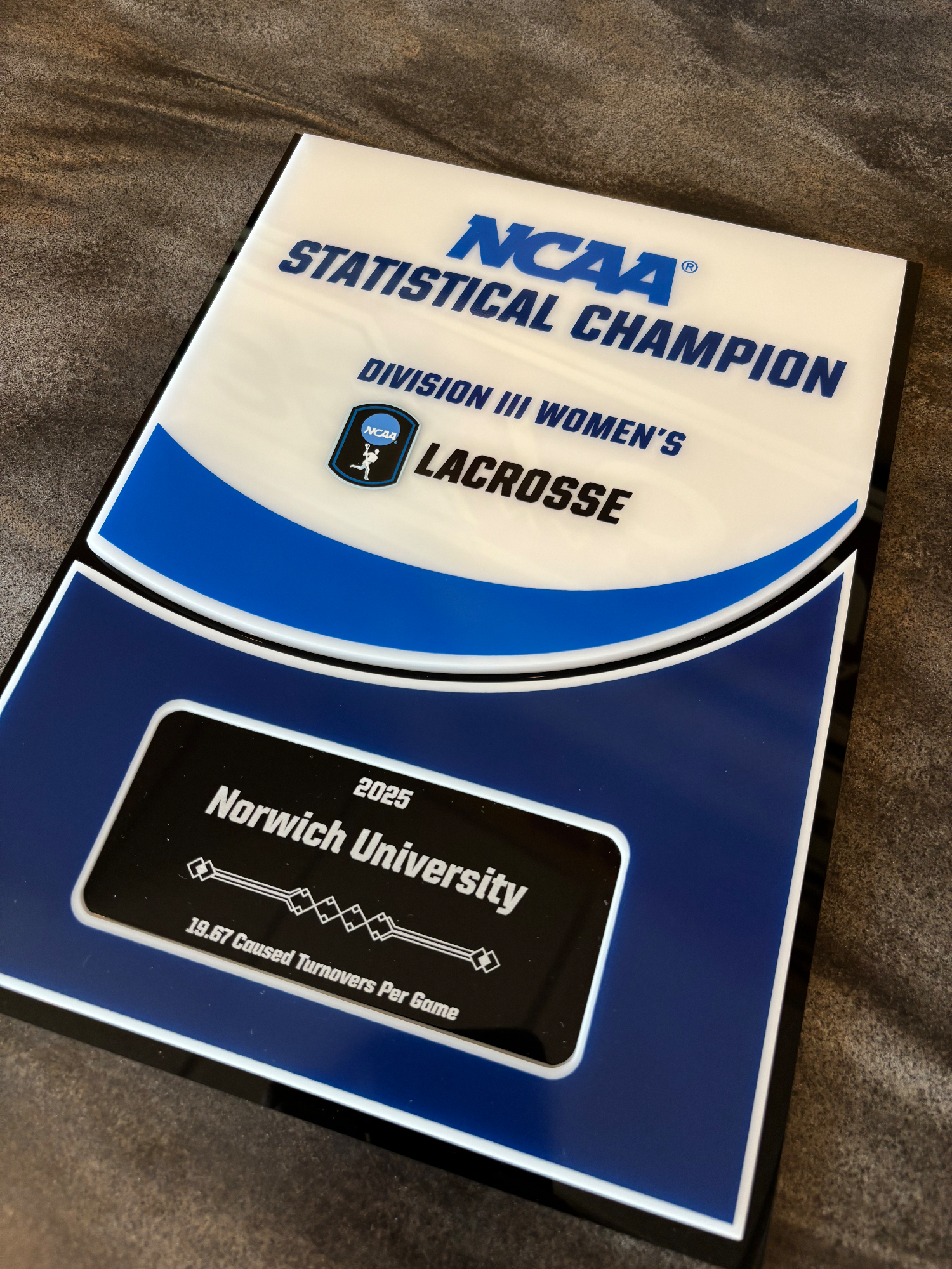 The NCAA Statistical Champion plaque lays on a counter, offset slightly.