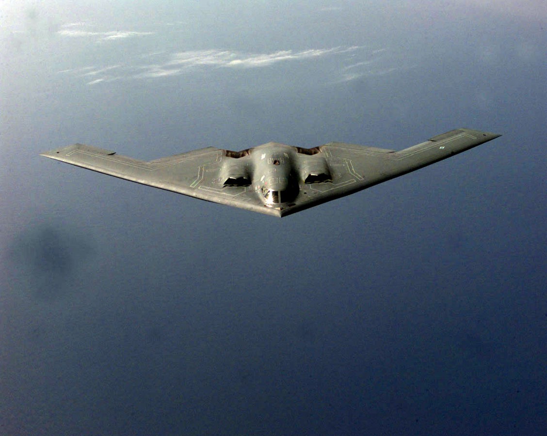 An overhead photo of a B-2 bomber flying over water.
