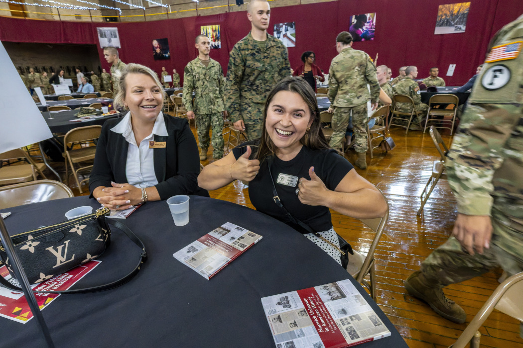 A Norwich student grins and gives two thumbs up during the First Contact event as a group of cadets walks behind her.