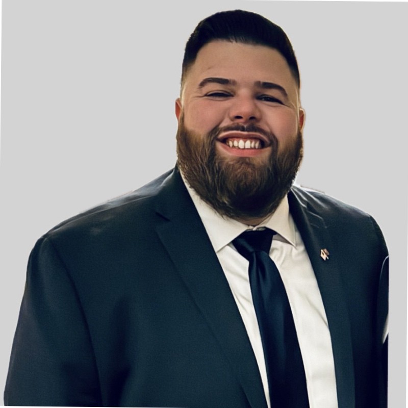 A man in a blue suit and tie with white shirt smiles in a professional headshot.