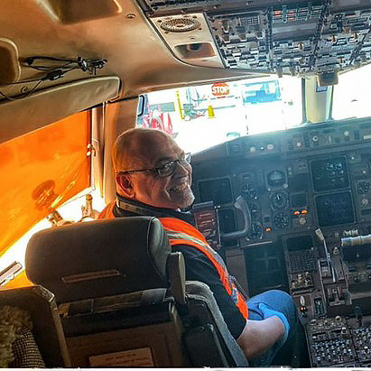 A man sits in the cockpit of a plane, smiling.