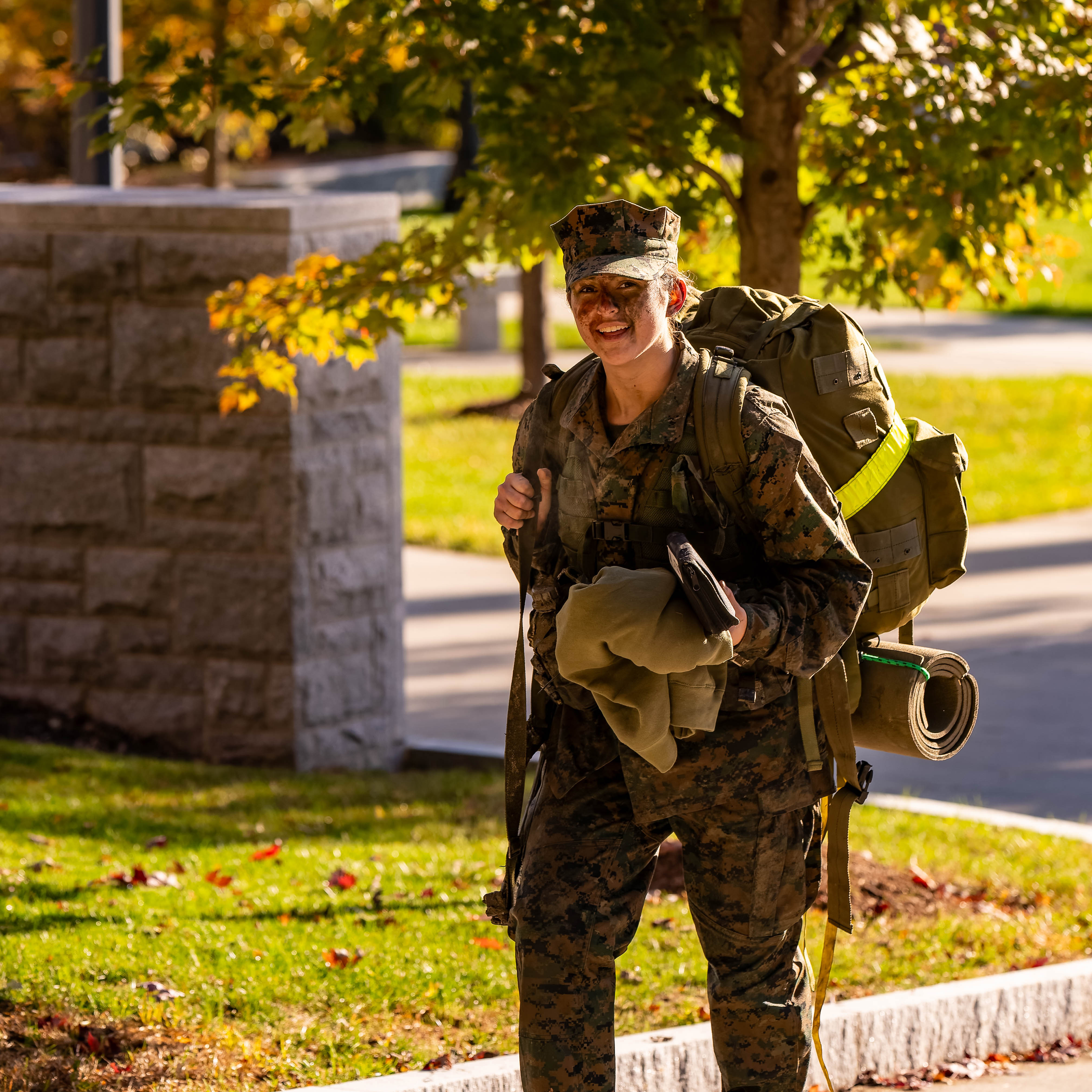 A smiling cadet in uniform walks across campus.