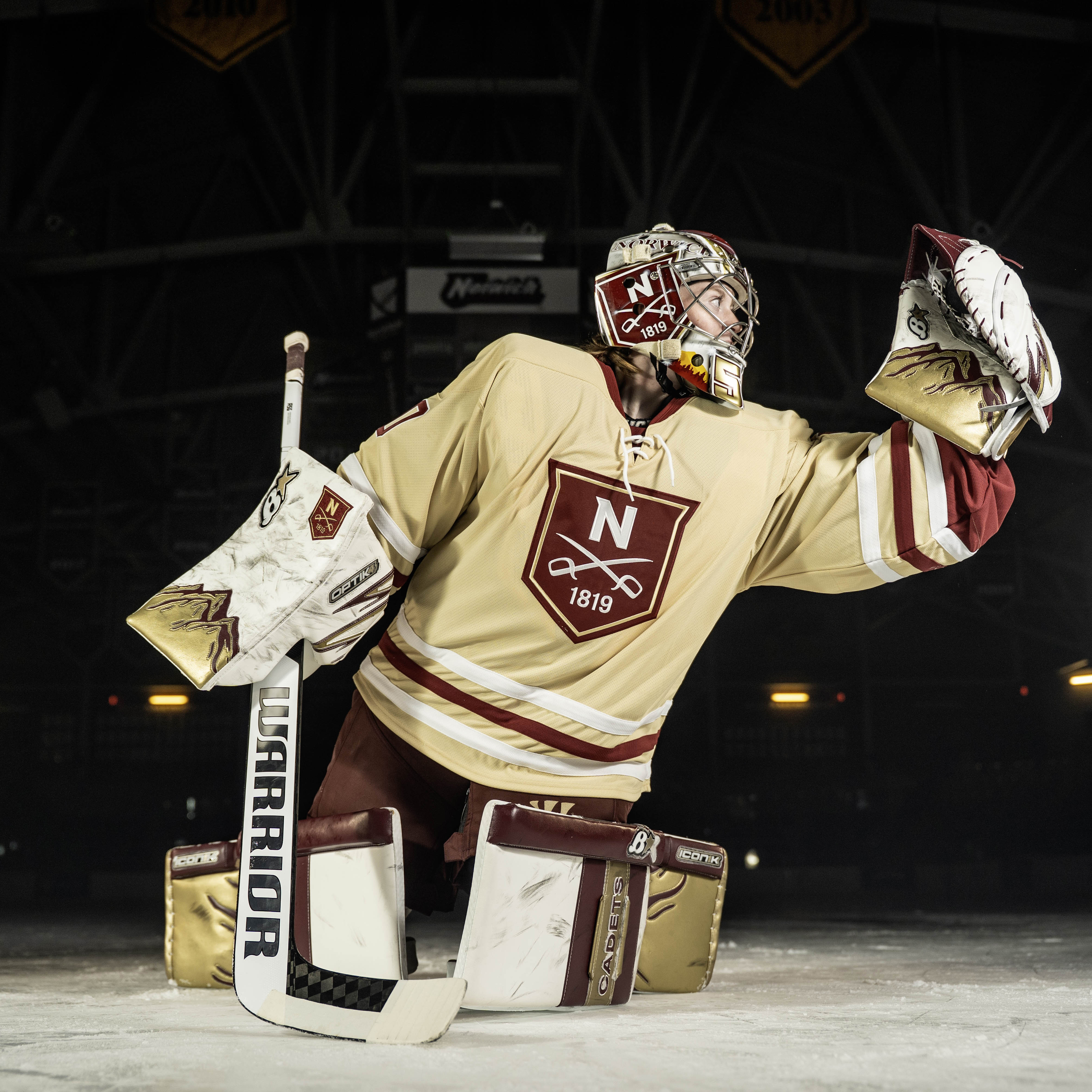 A hockey goalie takes a posed photo with the scoreboard in the background.