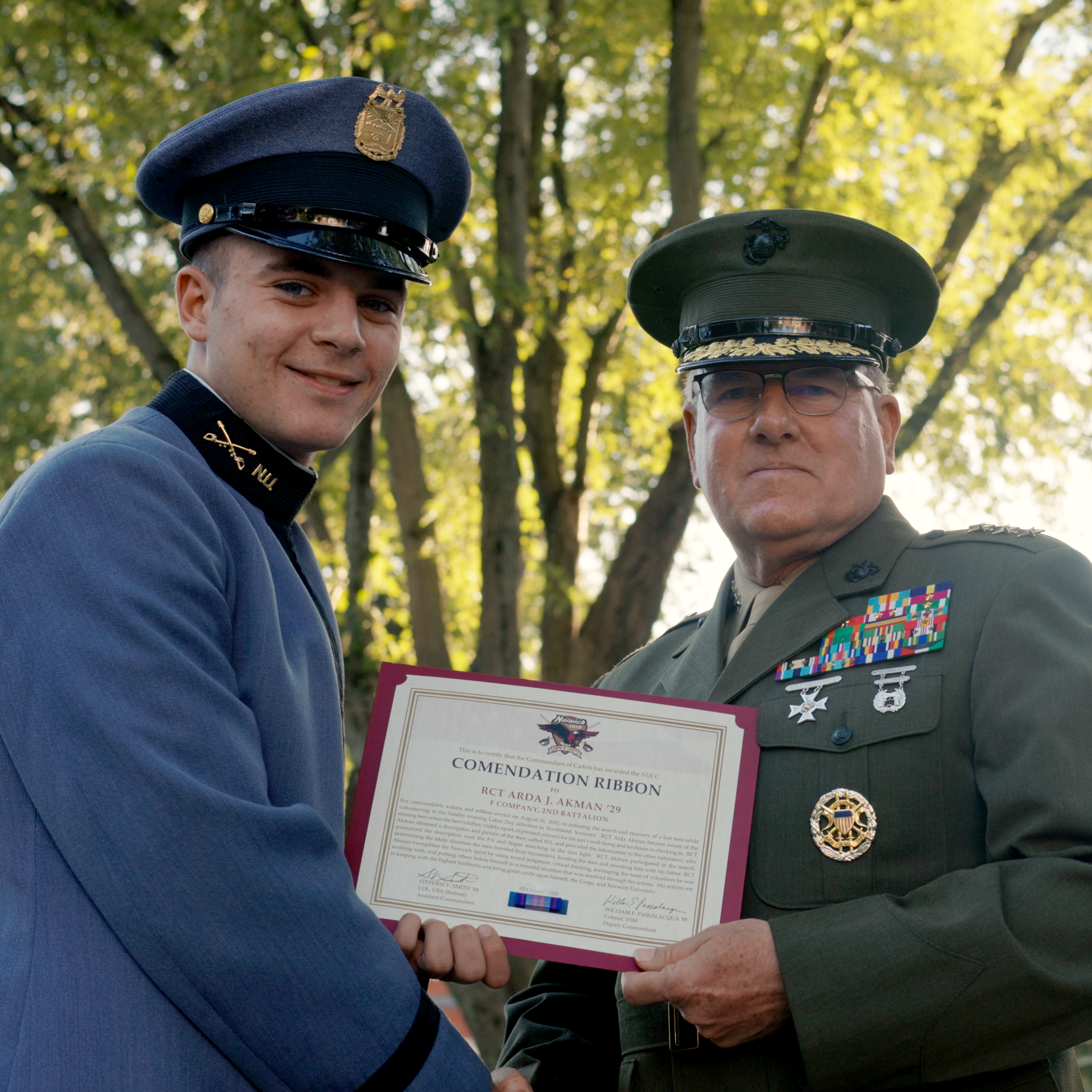 Two uniformed service members stand outdoors holding a commendation certificate together.