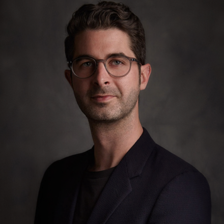 Formal headshot of a man in glasses and black attire.
