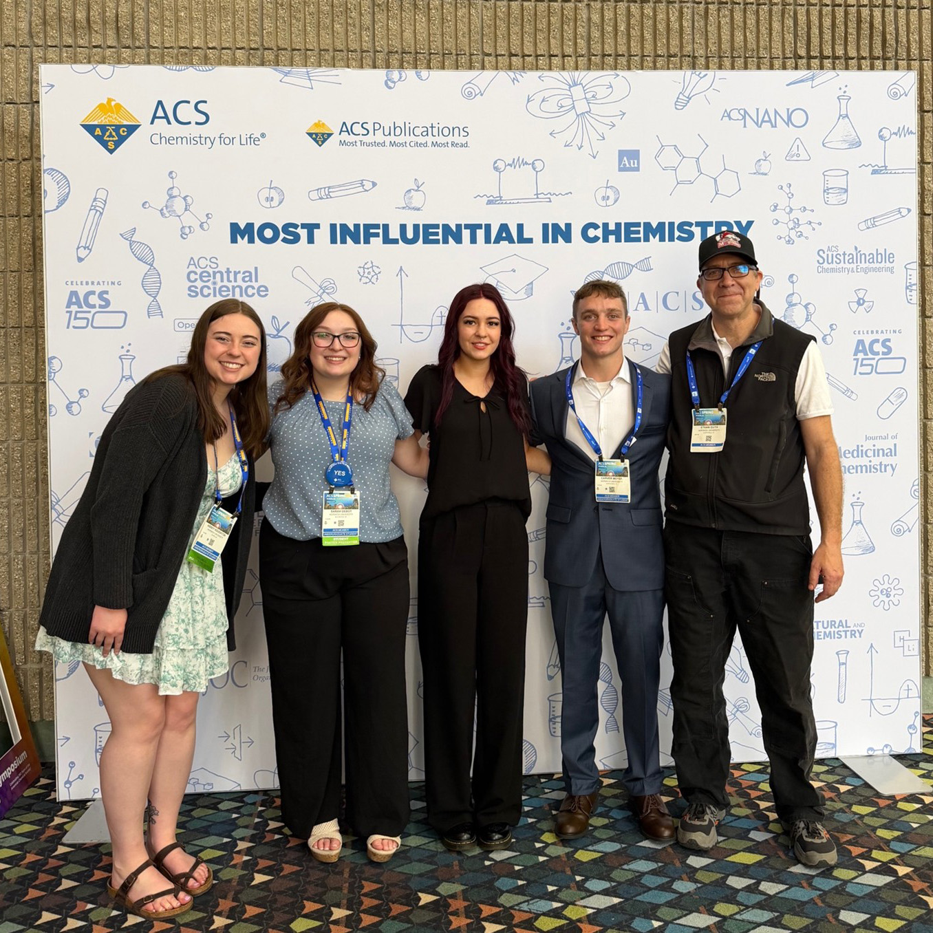 Five people pose with conference badges in front of an ACS Chemistry for Life backdrop.
