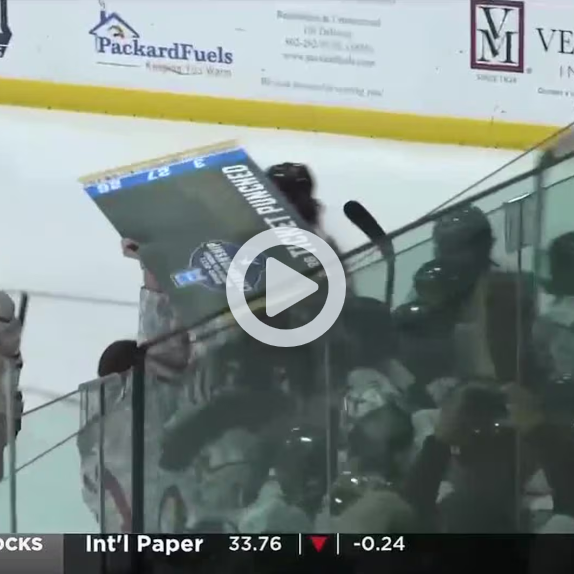 Hockey player holds a championship sign above the bench beside the rink glass.