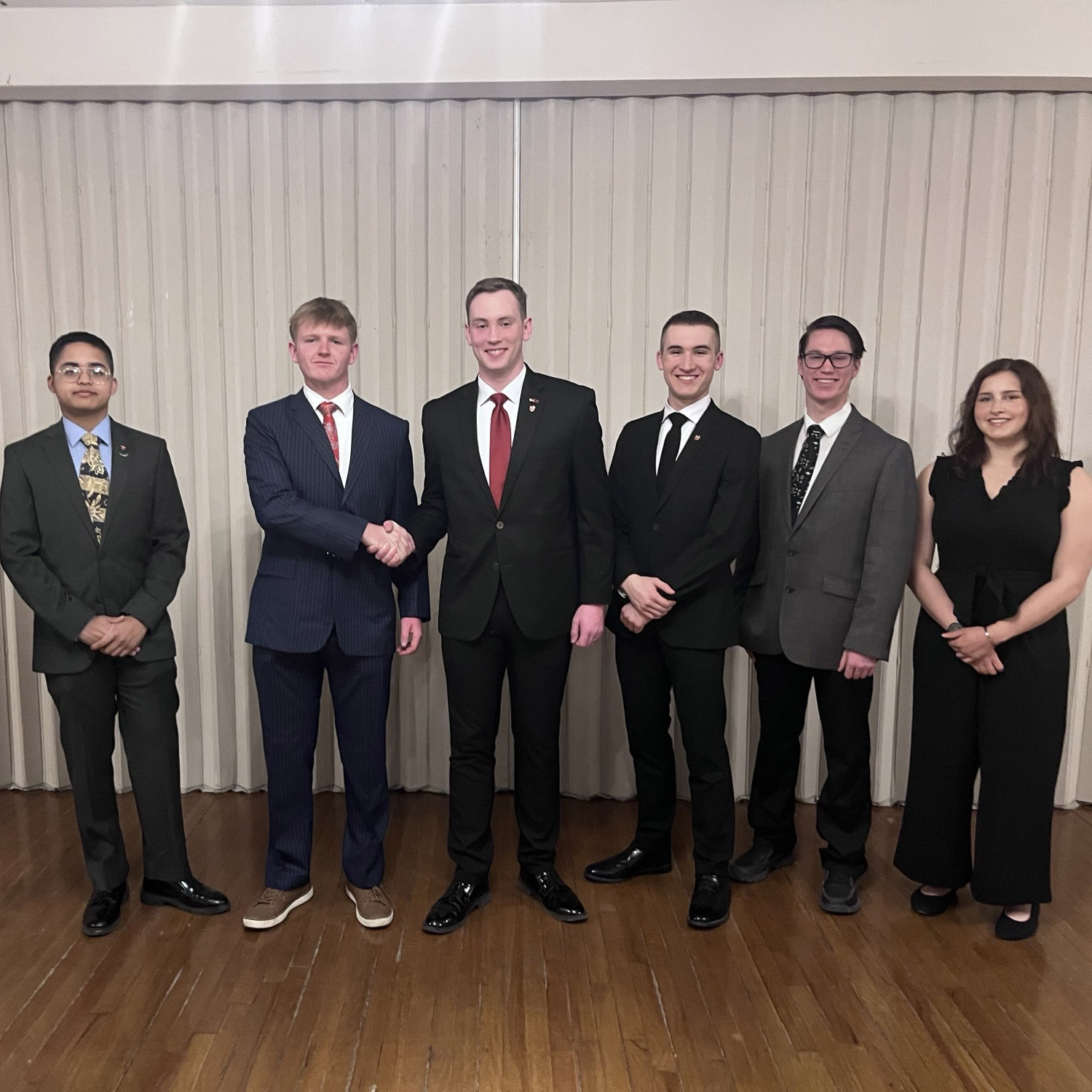 people in formal attire stand in a line as two men in the center shake hands.