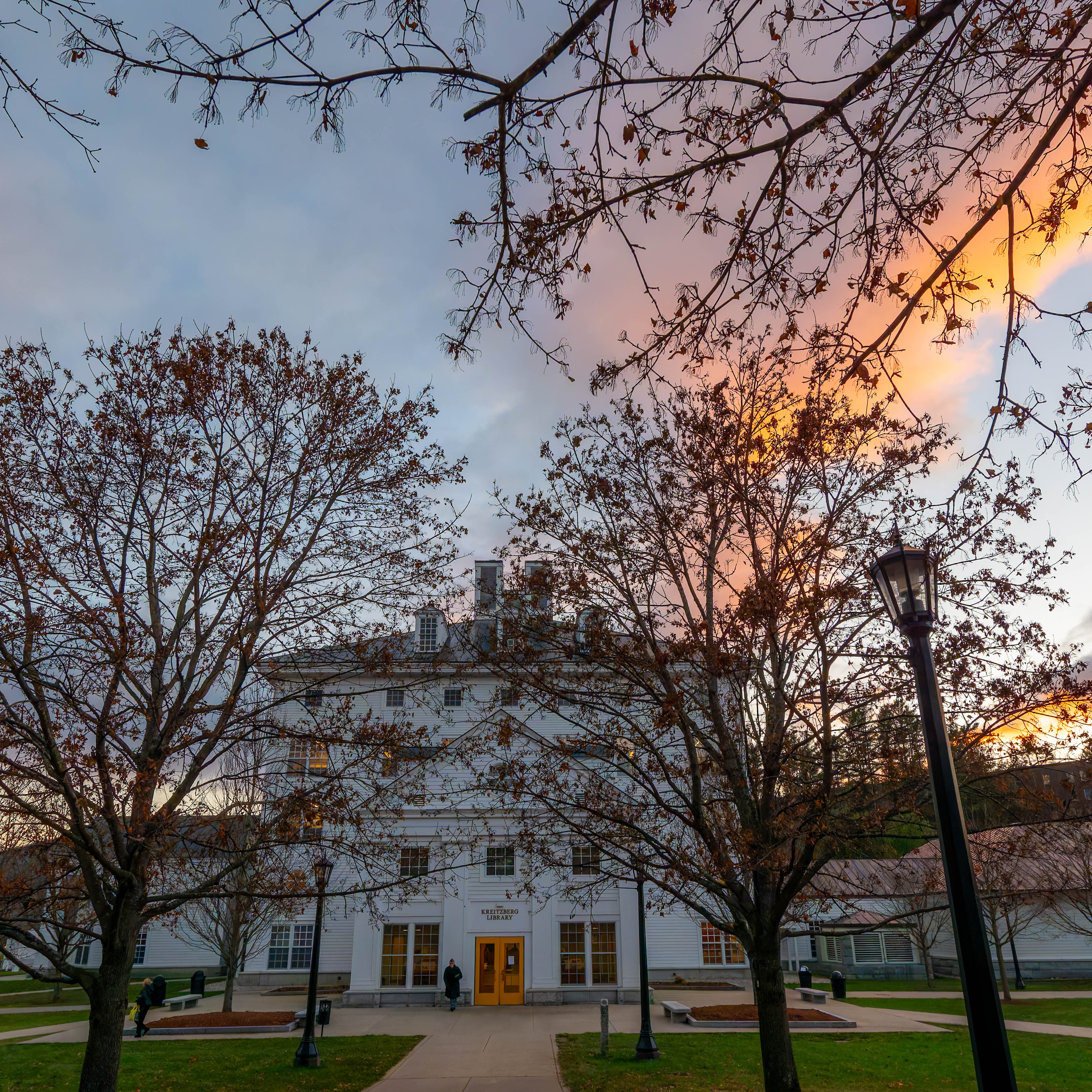 Kreitzberg Library stands behind leafless trees under a colorful evening sky