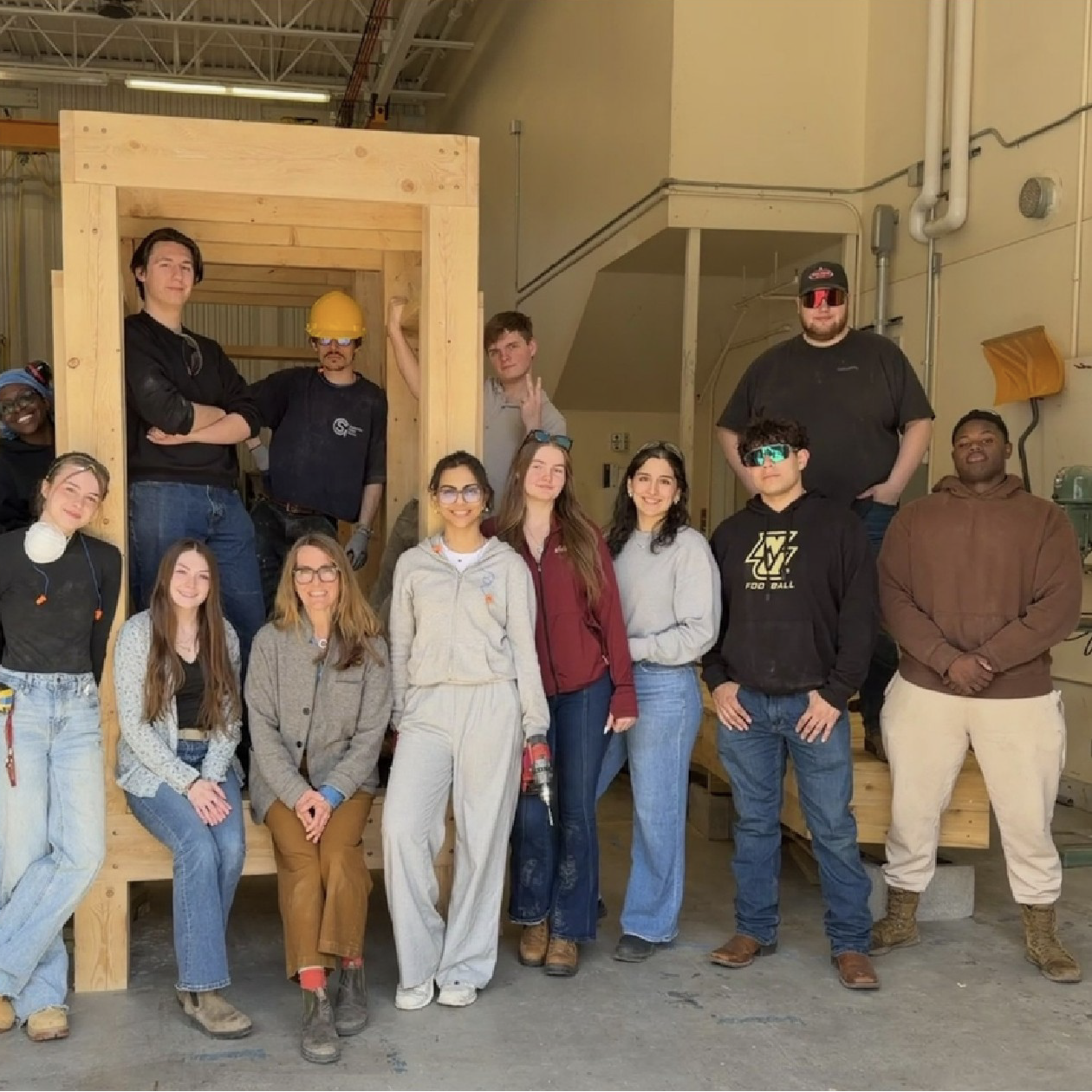 Students and an instructor pose beside a framed wood structure inside a construction lab