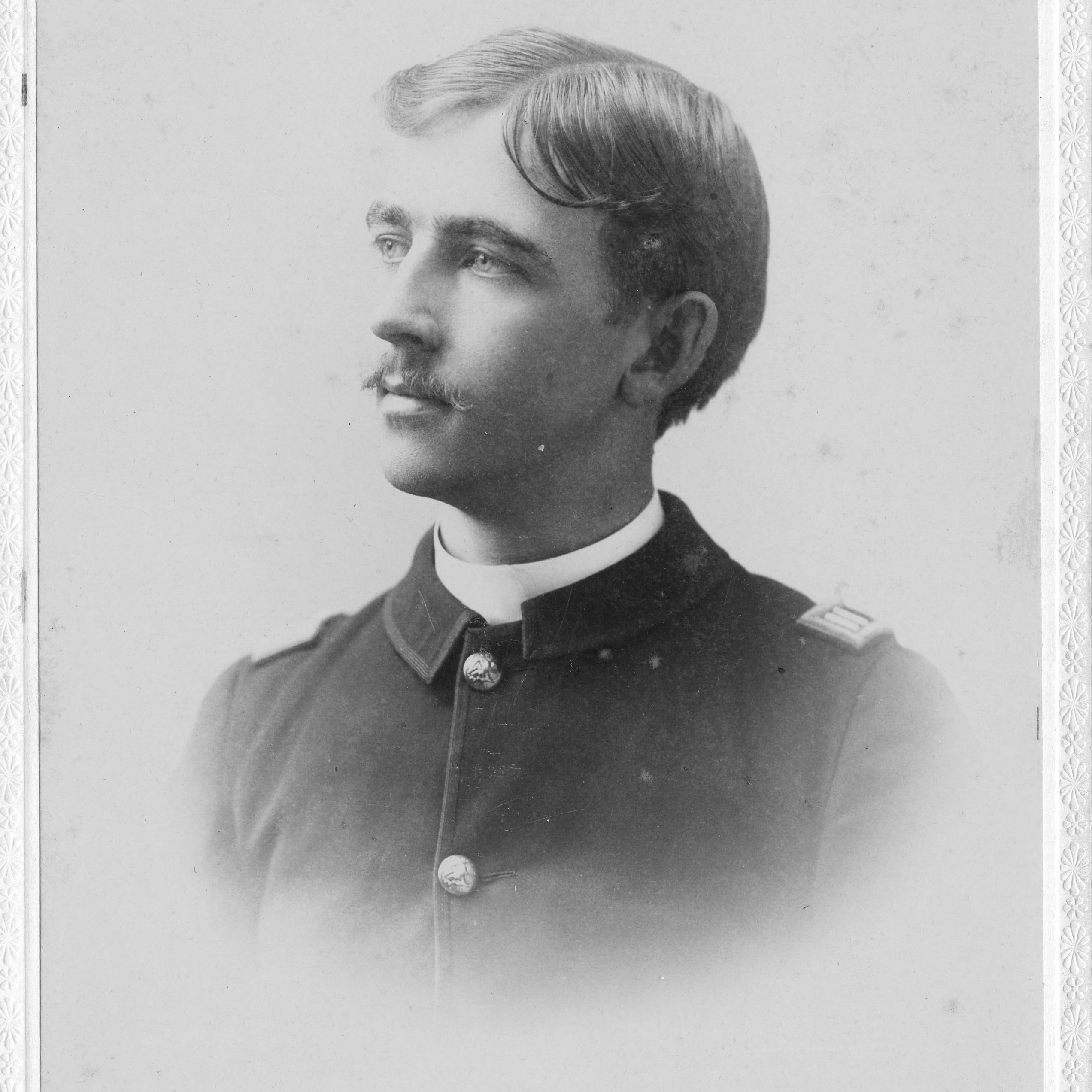 Service member in a dark uniform poses in profile for a studio portrait.