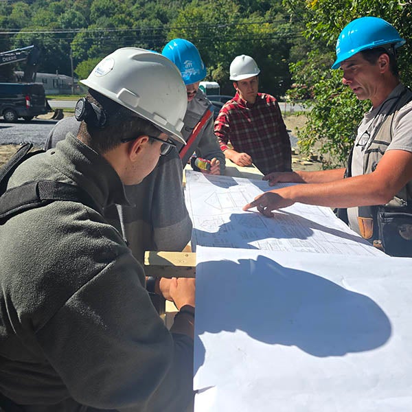 Four people in hard hats review building plans together at a construction site.