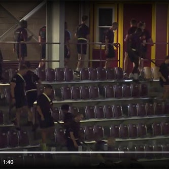 Students in matching shirts walk through stadium seating and gather near a doorway.