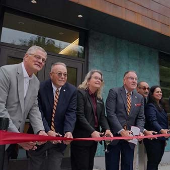 Six people cut a red ribbon outside the Cyber Fusion Center.