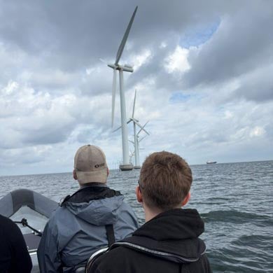 Two people ride in a boat toward offshore wind turbines.