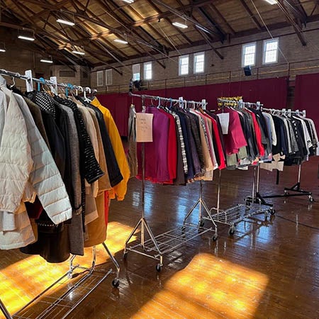 Clothing hangs on several rolling racks inside a large hall.