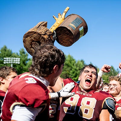 Norwich football players celebrate as one player holds a broken wooden trophy overhead.
