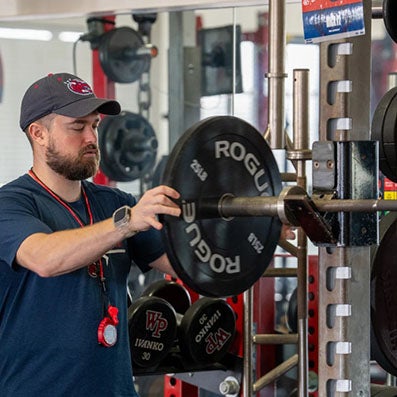 A person places a weight plate on a barbell in a gym.