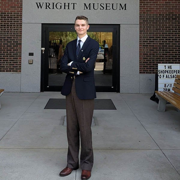 A person in a blazer stands with arms crossed outside the Wright Museum entrance.
