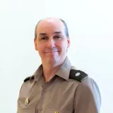 Person in a gray uniform shirt with insignia poses against a plain light background.