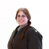 Person with glasses and a braid wears a dark coat and faces the camera.