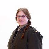 Person with glasses and a braid wears a dark coat and faces the camera.