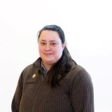 Person with long hair wears a dark sweater and faces the camera against a white background.