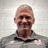 Portrait of a person wearing a Norwich shirt against a white brick wall.
