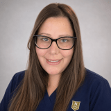 Person wearing navy Norwich University School of Nursing scrubs and glasses.