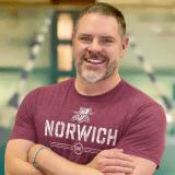 Portrait of a person wearing a Norwich T-shirt with arms crossed.