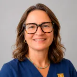 A person wearing glasses and blue Norwich University scrubs poses against a gray background.