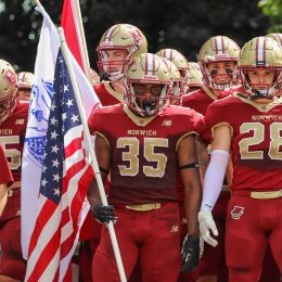 Jehric hackney stands in the center of his team while holding an American flag and preparing to run onto the football field.
