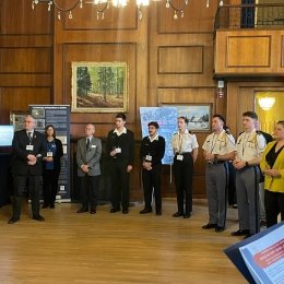 Group of individuals in professional attire standing in a wood-paneled room, with paintings and informational posters on display.