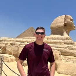Person in sunglasses and a t-shirt standing in front of the Sphinx and a pyramid in Egypt.