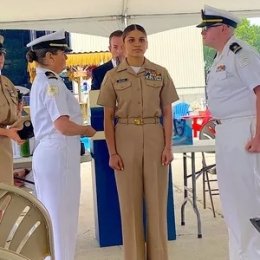 U.S. Navy officers in uniform participating in a formal ceremony under a tent.