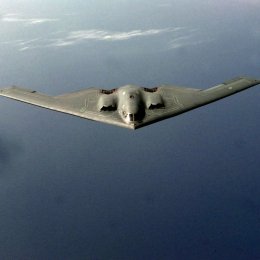 An overhead photo of a B-2 bomber flying over water.