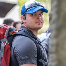 Jayden LaVecchia stands with a hat and sunglasses on top, in a polo wearing a backpack looking over his right shoulder.
