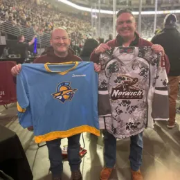 An image of two NU Alumni holding hockey jerseys, for the Atlanta Gladiators and the Norwich Cadets