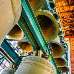 Large bells hang in a bell tower beneath a wooden ceiling.