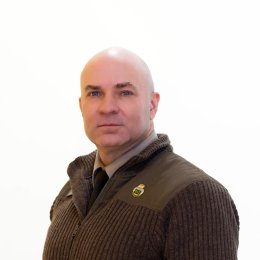 Person in a dark zip-up sweater and tie faces the camera against a white background.